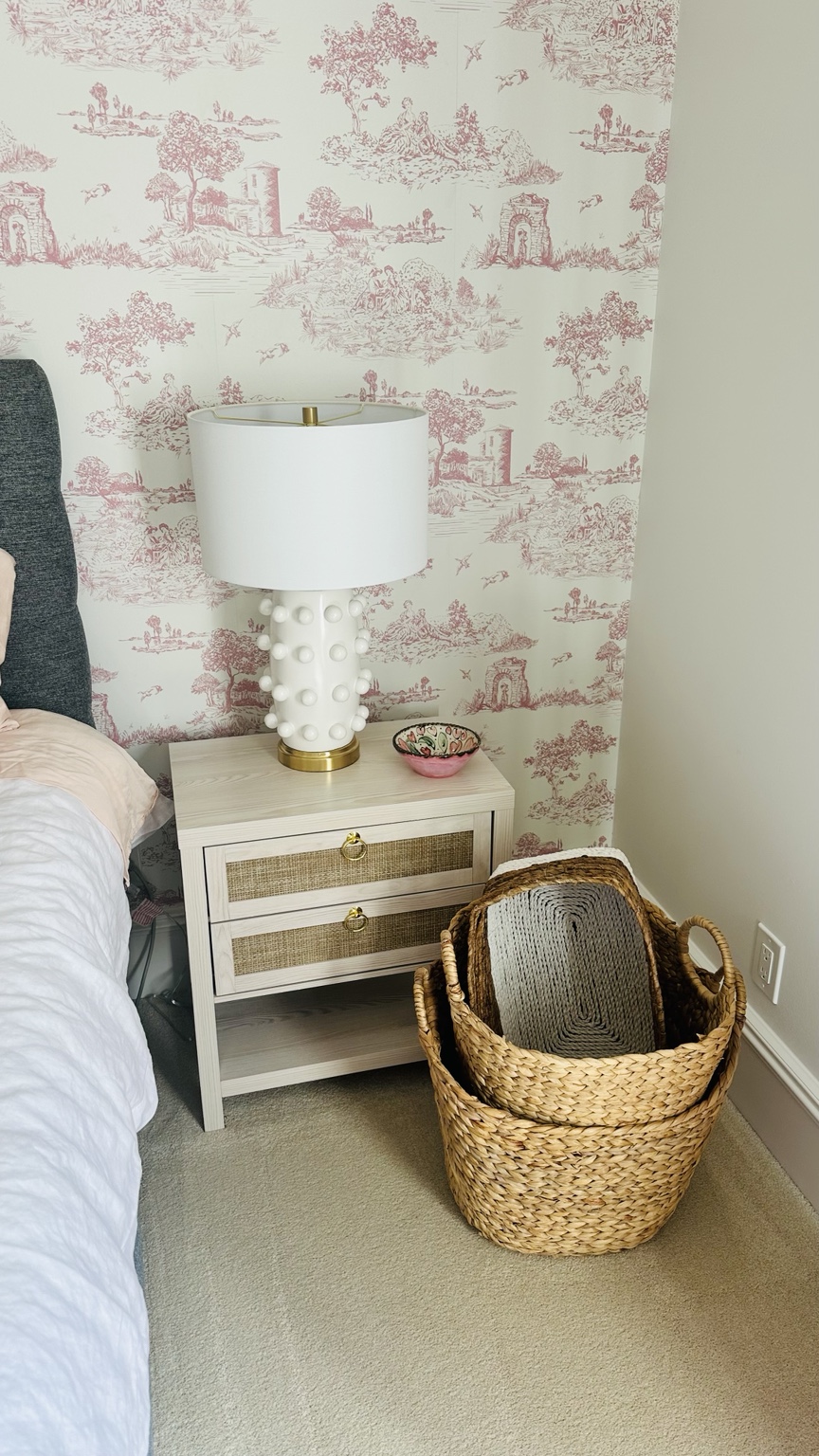A finished pink toile bedroom corner with lamp and rattan nightstand