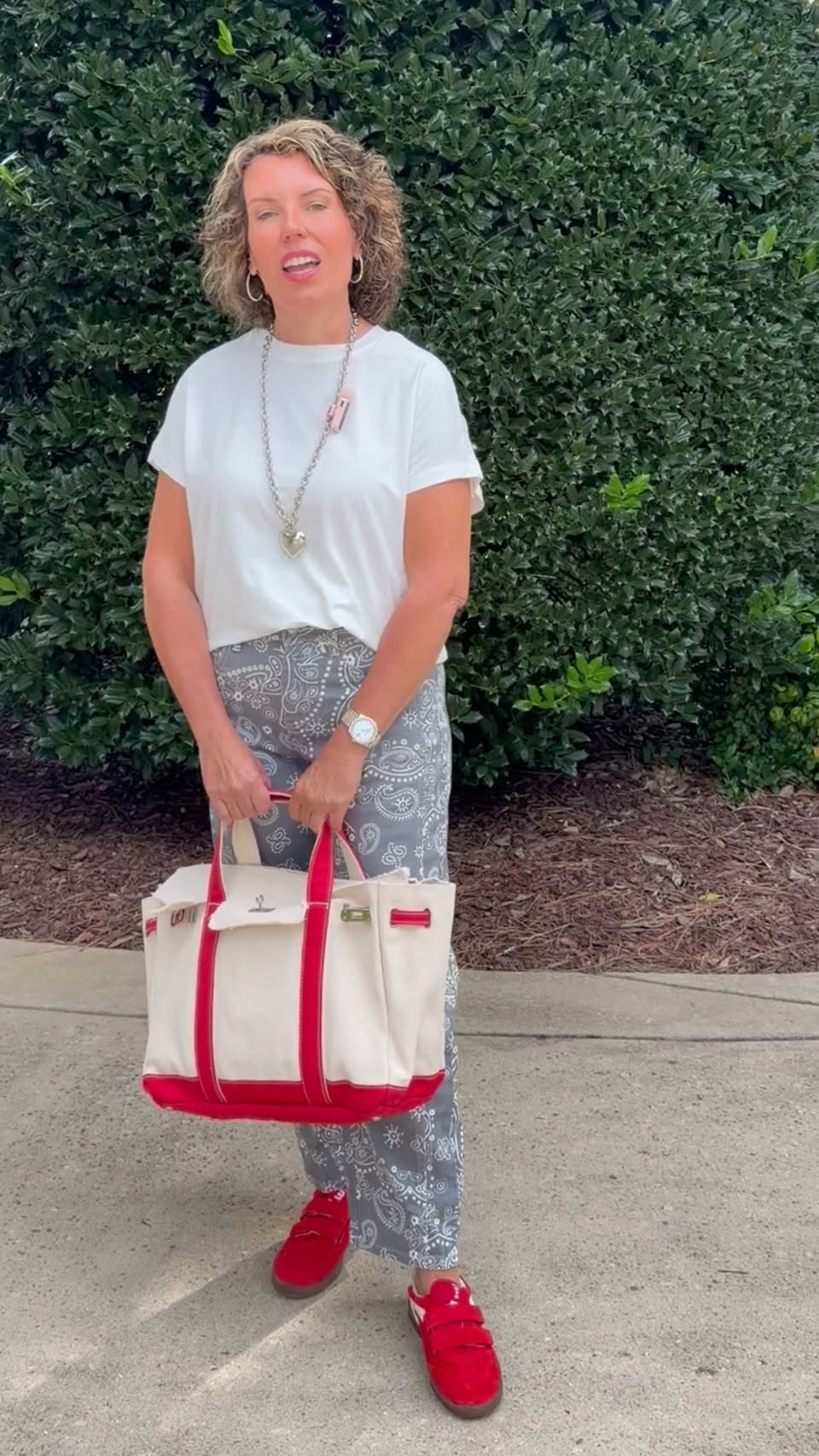 Jessica wearing a white tee, gray paisley pants, and red sneakers while carrying a red-trim canvas tote