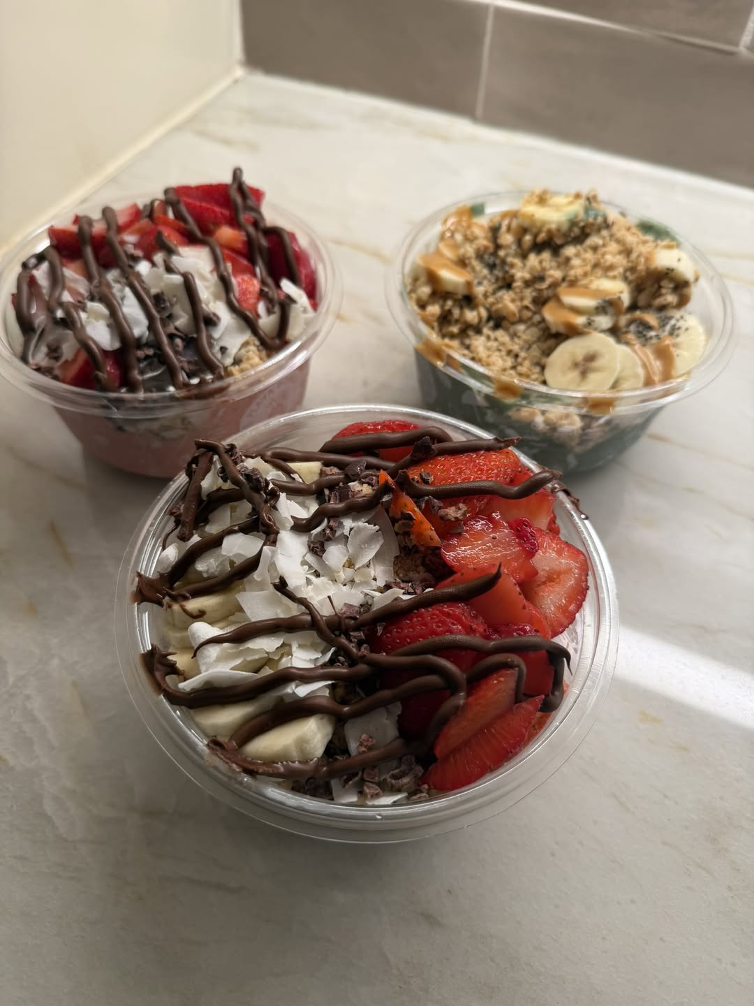 Three colorful Playa Bowls topped with strawberries, banana, coconut, chocolate, granola, and nut butter